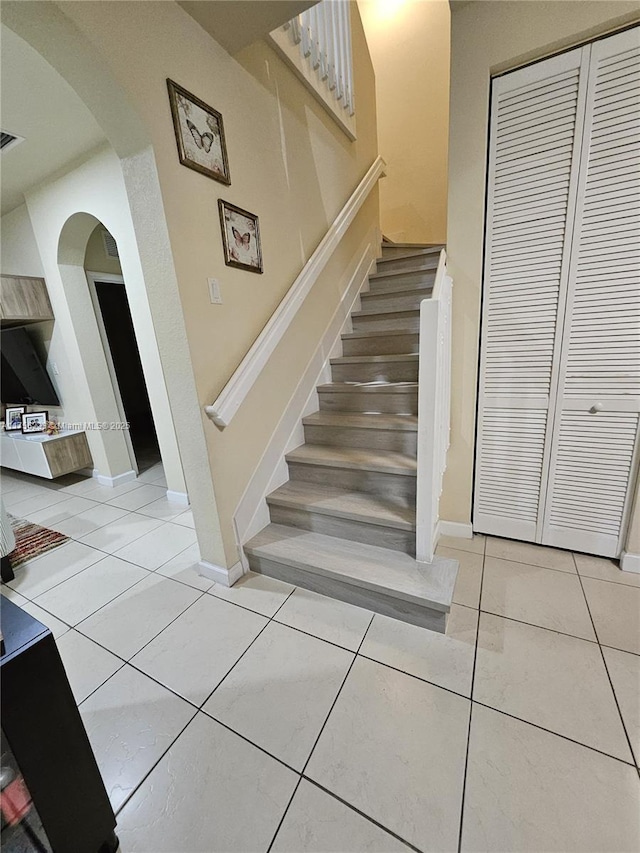 staircase with tile patterned flooring, arched walkways, and baseboards