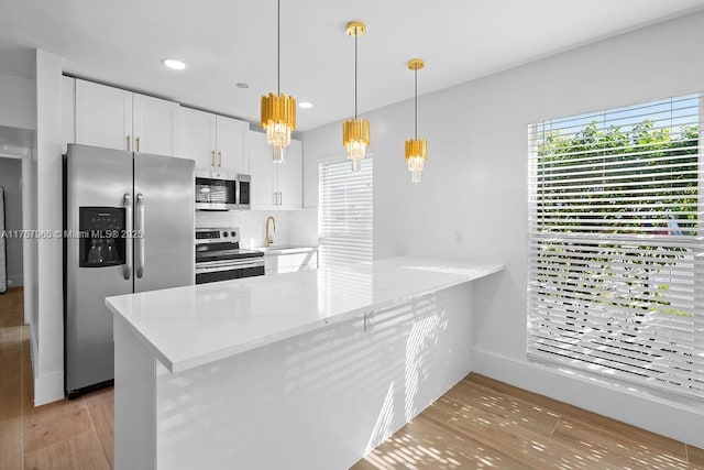 kitchen featuring a peninsula, light wood-style floors, white cabinets, appliances with stainless steel finishes, and decorative light fixtures