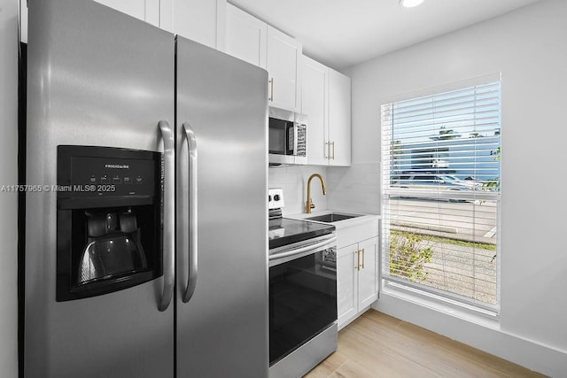 kitchen featuring stainless steel appliances, a sink, white cabinetry, light wood-type flooring, and decorative backsplash