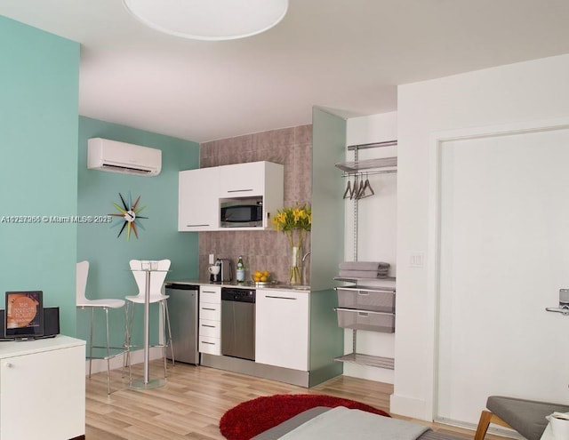 kitchen featuring light wood-style flooring, stainless steel appliances, white cabinets, tasteful backsplash, and a wall mounted air conditioner