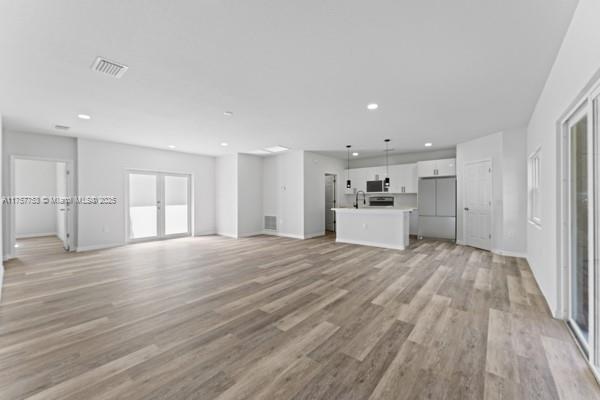 unfurnished living room featuring baseboards, light wood-type flooring, visible vents, and recessed lighting