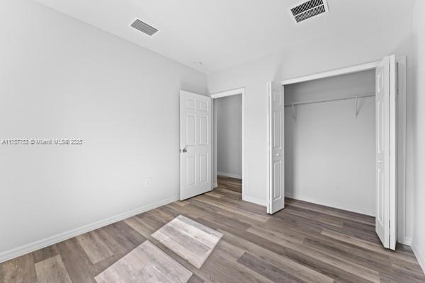 unfurnished bedroom with a closet, wood finished floors, visible vents, and baseboards