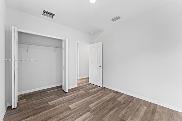 unfurnished bedroom featuring baseboards, a closet, visible vents, and wood finished floors