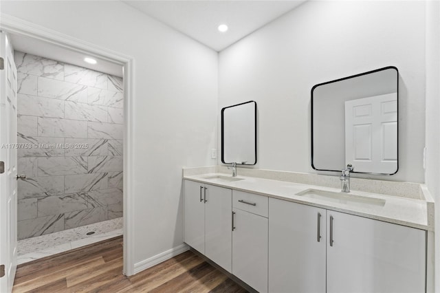 full bathroom with a walk in shower, double vanity, a sink, and wood finished floors