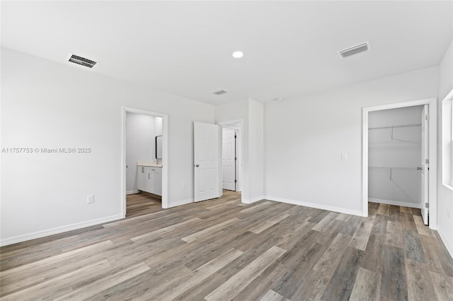 unfurnished bedroom featuring light wood-style floors, a walk in closet, visible vents, and baseboards