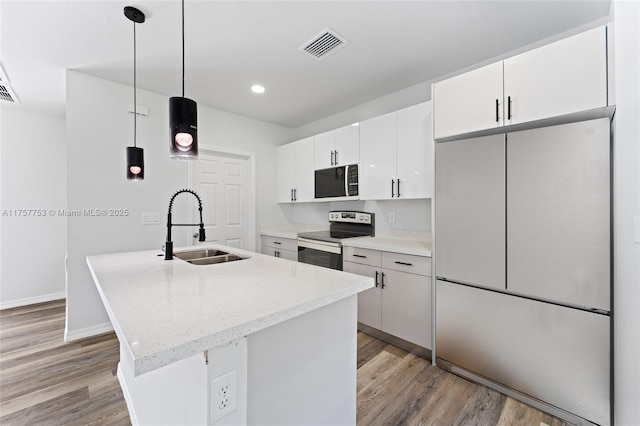 kitchen featuring electric range, visible vents, an island with sink, refrigerator, and a sink