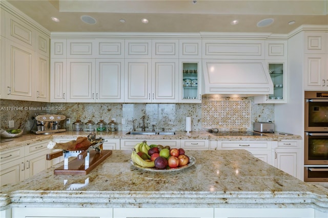 kitchen with black electric stovetop, stainless steel double oven, custom exhaust hood, backsplash, and light stone countertops