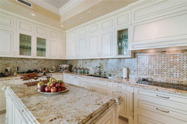 kitchen with light stone counters, black cooktop, a sink, backsplash, and crown molding