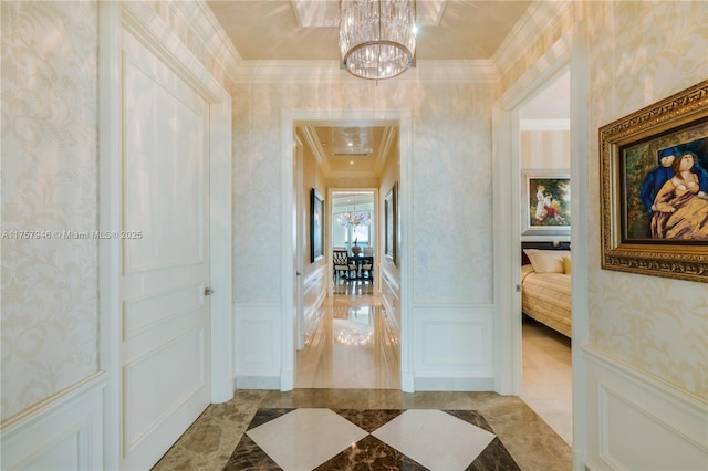 corridor featuring wallpapered walls, wainscoting, ornamental molding, a decorative wall, and a notable chandelier