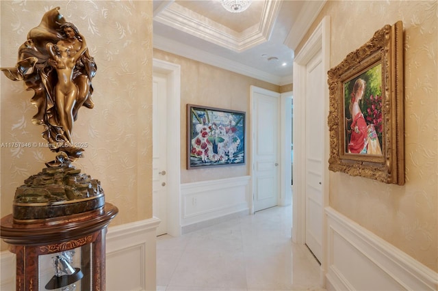 corridor featuring crown molding, light tile patterned floors, a wainscoted wall, and a decorative wall