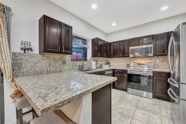 kitchen featuring decorative backsplash, appliances with stainless steel finishes, a peninsula, dark brown cabinets, and a sink