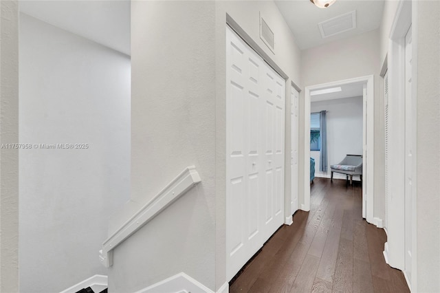 hallway featuring dark wood-style floors, baseboards, visible vents, and an upstairs landing