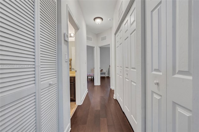 hall with visible vents, baseboards, and dark wood-type flooring