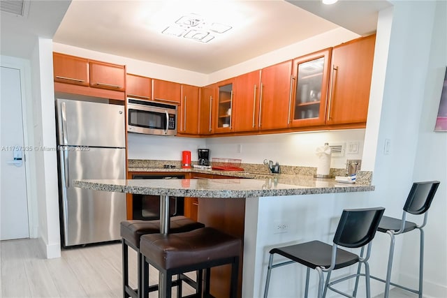 kitchen featuring visible vents, brown cabinetry, glass insert cabinets, a peninsula, and stainless steel appliances