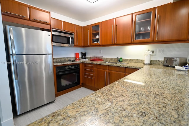 kitchen featuring a toaster, glass insert cabinets, a sink, light stone countertops, and black appliances