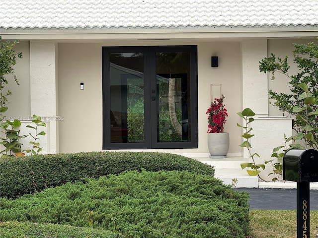 view of exterior entry featuring a tile roof, french doors, and stucco siding