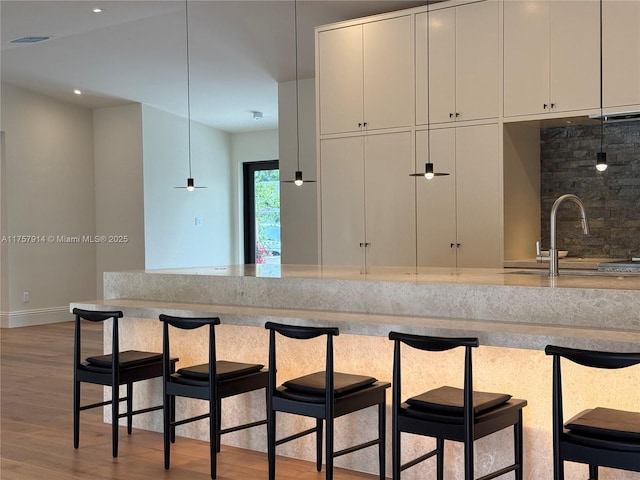 kitchen with a breakfast bar, a sink, white cabinets, backsplash, and light wood finished floors