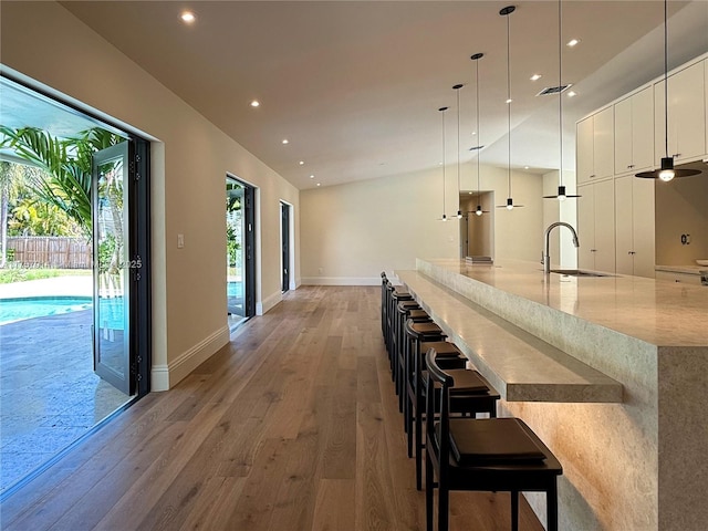 hall featuring baseboards, visible vents, light wood-type flooring, a sink, and recessed lighting