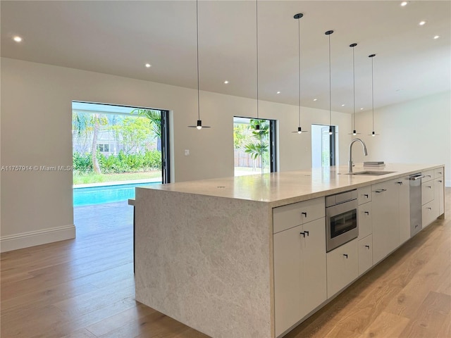 kitchen with a spacious island, light wood-type flooring, a healthy amount of sunlight, and a sink