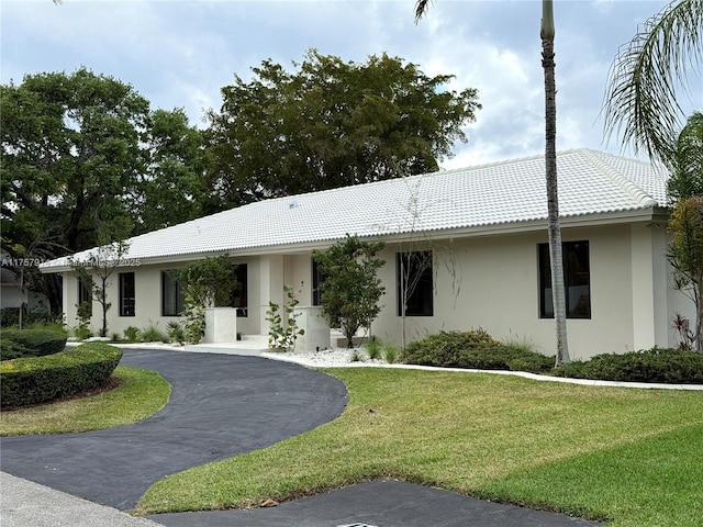 single story home featuring a tile roof, a front lawn, and stucco siding