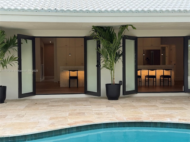 view of exterior entry featuring a patio area, an outdoor pool, and a tiled roof