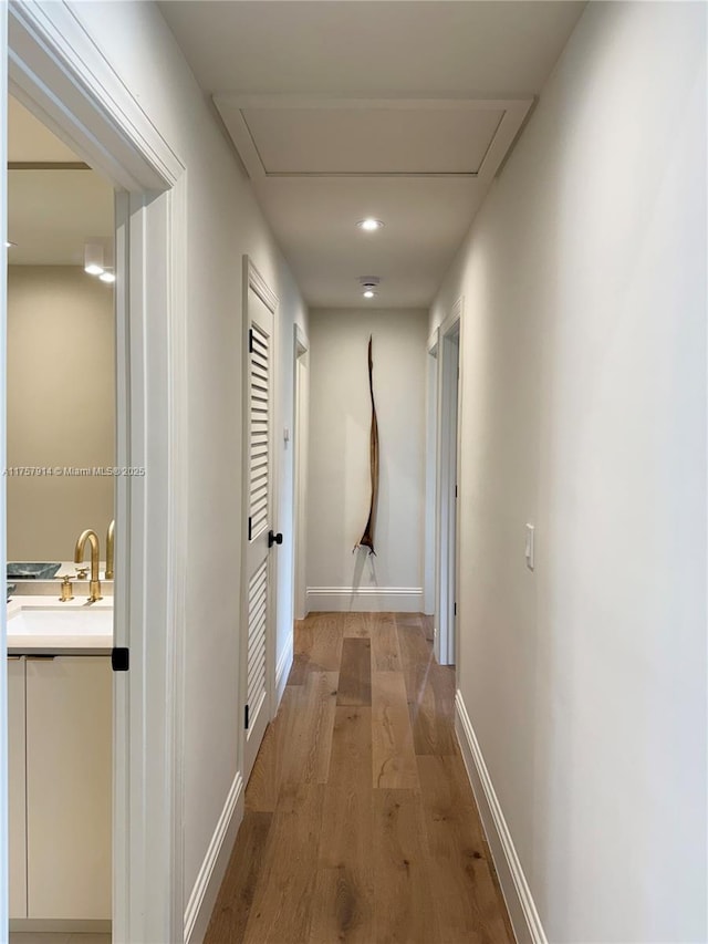 corridor featuring light wood-style floors, attic access, a sink, and baseboards