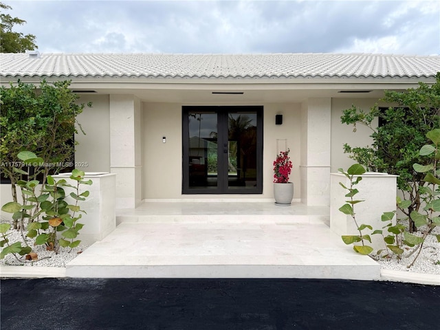 doorway to property featuring covered porch, french doors, a tile roof, and stucco siding