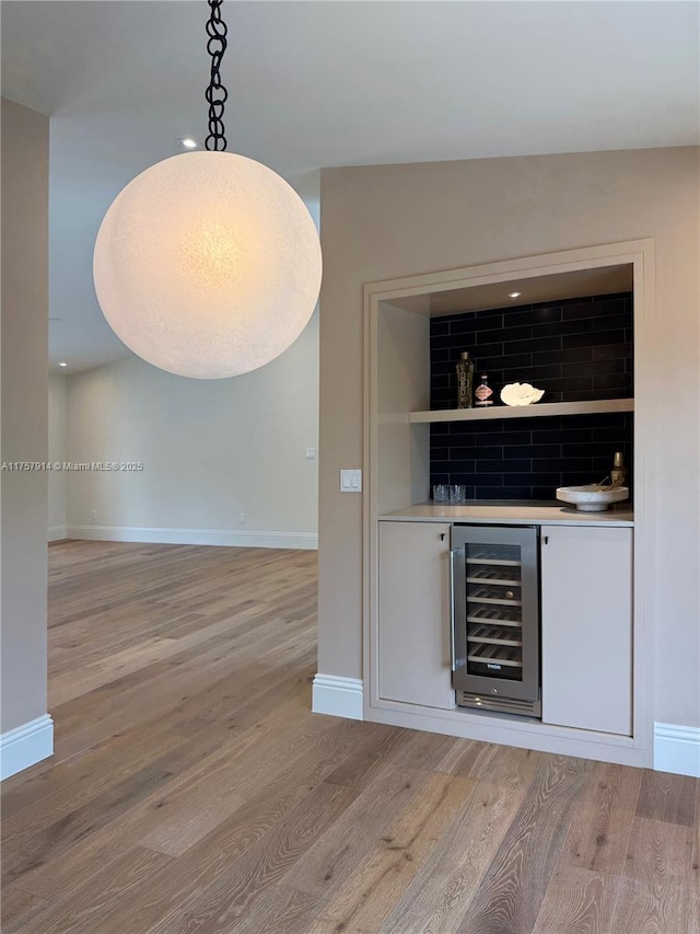 bar with wine cooler, a dry bar, hanging light fixtures, light wood-type flooring, and baseboards