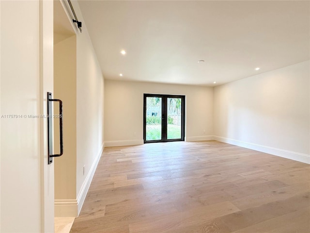 spare room with a barn door, recessed lighting, baseboards, french doors, and light wood-type flooring