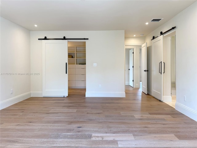 spare room with light wood finished floors, a barn door, visible vents, and baseboards