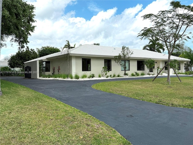 single story home with aphalt driveway, a tile roof, a front lawn, and stucco siding