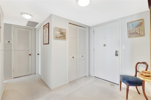 foyer entrance featuring light colored carpet, visible vents, and baseboards