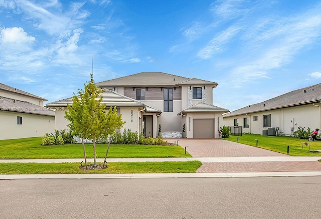 view of front of house with a front yard, decorative driveway, central AC, and stucco siding