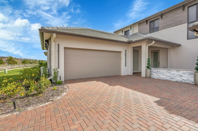 view of front of property featuring a tiled roof, decorative driveway, an attached garage, and stucco siding