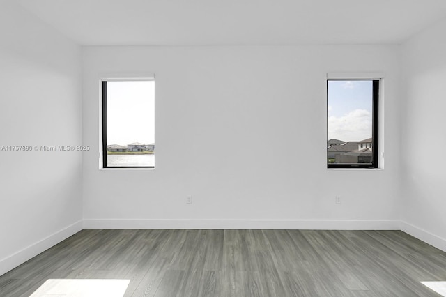 empty room with baseboards, wood finished floors, and a healthy amount of sunlight