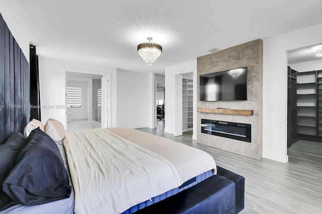 bedroom featuring a notable chandelier, a fireplace, wood finished floors, visible vents, and a walk in closet