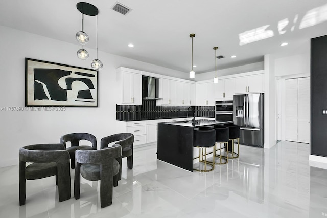 kitchen with a breakfast bar area, visible vents, appliances with stainless steel finishes, white cabinets, and wall chimney range hood