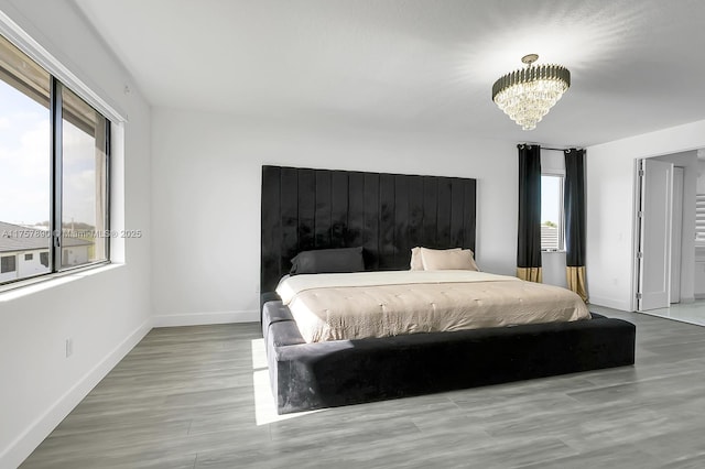 bedroom with multiple windows, baseboards, a notable chandelier, and wood finished floors