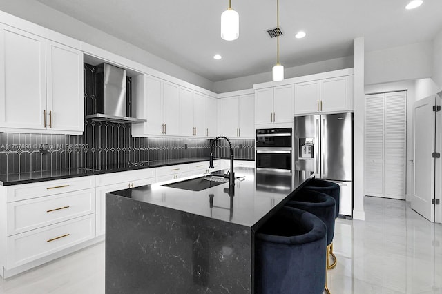 kitchen featuring stainless steel refrigerator with ice dispenser, visible vents, multiple ovens, a sink, and wall chimney range hood