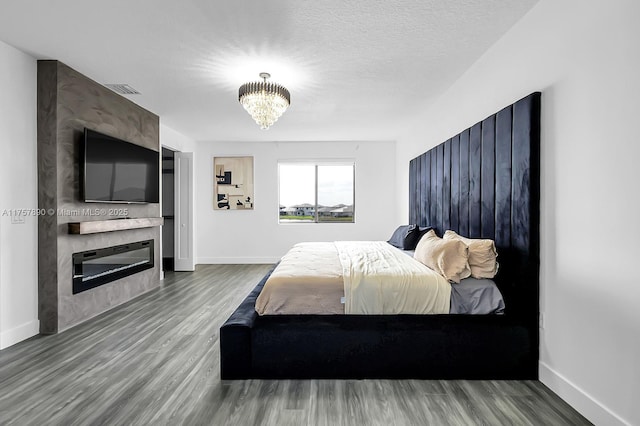 bedroom with a large fireplace, a textured ceiling, baseboards, and wood finished floors