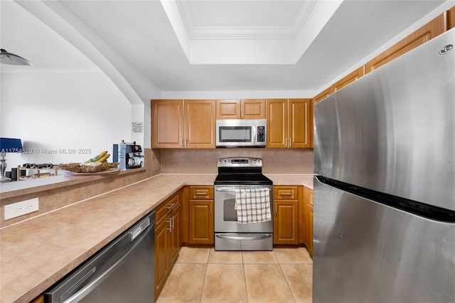 kitchen with a tray ceiling, light tile patterned floors, stainless steel appliances, light countertops, and ornamental molding