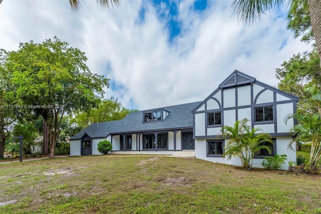 english style home with roof with shingles, a front lawn, and stucco siding