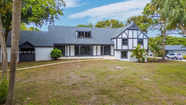 tudor home featuring roof with shingles and a front lawn