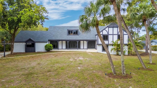 english style home with a front lawn, roof with shingles, a sunroom, and stucco siding