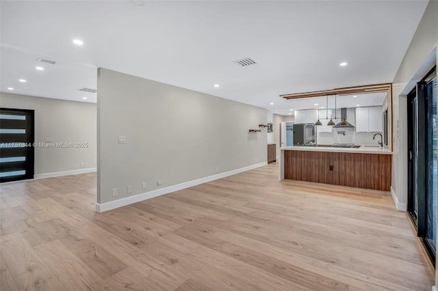 kitchen featuring open floor plan, white cabinetry, a sink, and wall chimney range hood