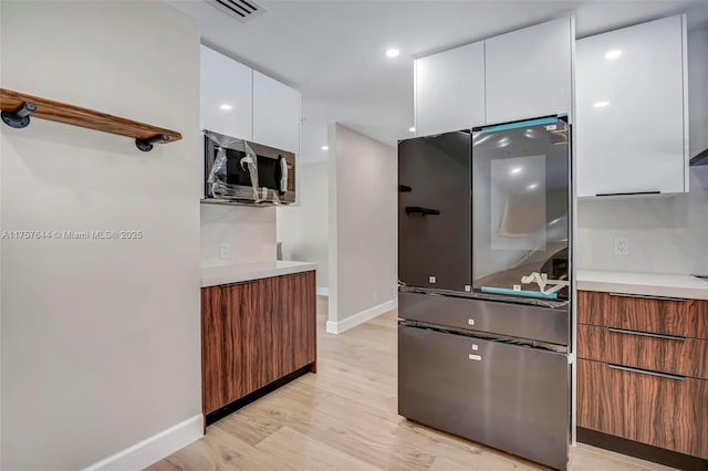 kitchen featuring light wood finished floors, light countertops, stainless steel microwave, white cabinetry, and modern cabinets