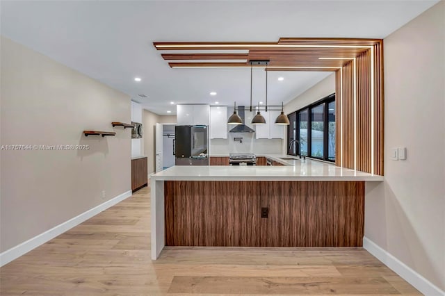 kitchen featuring stainless steel range with electric cooktop, a sink, wall chimney range hood, white cabinetry, and a peninsula