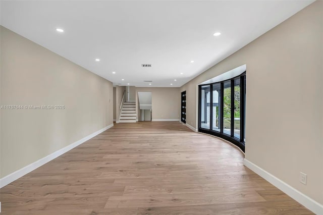 unfurnished room with light wood-type flooring, baseboards, visible vents, and stairway