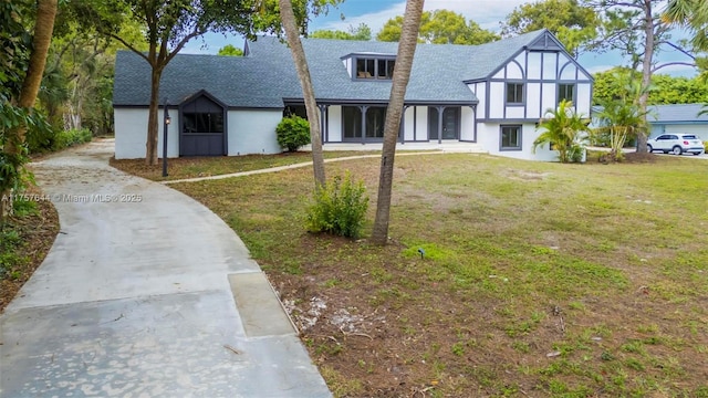 tudor-style house featuring driveway, a shingled roof, and a front yard