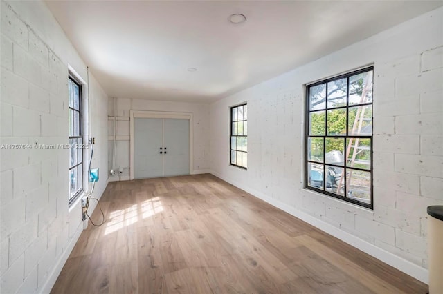 empty room featuring concrete block wall, light wood-style flooring, and baseboards